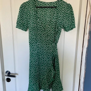 Somrig grön klänning - Söt, figursmickrande grön klänning. Knyte i midjan som framhäver kurvorna. Lite klarare grön färg än på bilderna. Använd 2 gånger och i superfint skick. Små vita blommor som mönster.