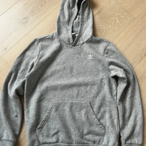 Grå hoodie adidas - Några fläckar finns det, men annars i gott skick. Fläckarna är på bröstet och en liten på ärmen. (Se bilden) Ungdomsstorlek 170