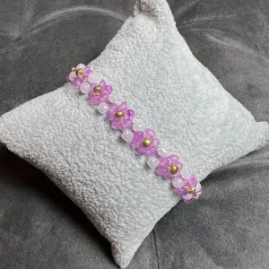 Egentillverkat pärlarmband med vackra rosa blommor, vita och guldfärgade pärlor och guldigt spänne. Justerbar passform mellan 18-20 cm.