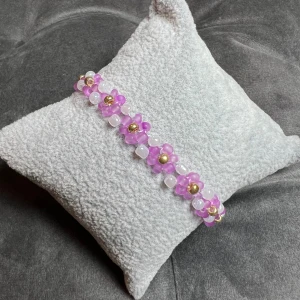 Pärlarmband  - Egentillverkat pärlarmband med vackra rosa blommor, vita och guldfärgade pärlor och guldigt spänne. Justerbar passform mellan 18-20 cm.