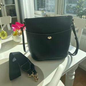 Svart väska  - Svart väska med två olika band (justerbara). Köpt på Åhléns, använd fåtal gånger. Innerfack med dragkedja och ytterfack.  Längd: 29cm Höjd: 27cm Kan skickas mot fraktkostnad alternativt hämtas/mötas upp i Stockholm💕