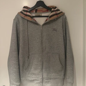 Burberry Hoodie - En stilren och riktigt snygg Hoodie från lyxmärket Burberry i färgen grå. Hoodie är i utmärkt skick (10/10) utan några som helst defekter. Bara att skriva vid funderingar!