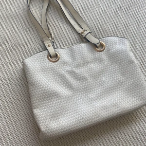 Fin vit läder väska i guldiga och svarta detaljer. - Vit väska som är sthlmstil med fina guldiga och svarta detaljer, har tre stora fack och tre mindre fickor. Obs några defekter.