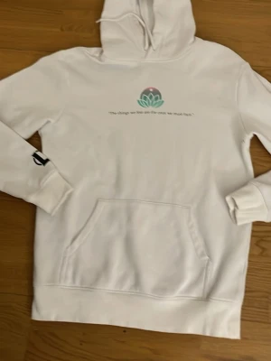 Vit hoodie med tryck och magficka - Säljer en vit hoodie från Champion med tryck på bröstet och texten 'The things we fear are the ones we must face.' Stor magficka framtill och ribbade muddar. Champion-logga på ärmen. Perfekt för chill dagar eller när du vill ha en clean look.