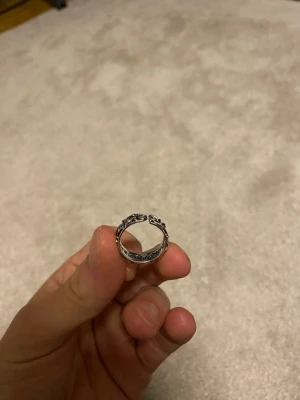 Chrome Hearts Justerbar Ring - Säljer en snygg Chrome Hearts ring med detaljerat bladmönster runt hela ringen. Ringen har en klassisk form och är tillverkad i metall med en antik finish som ger den en cool vintagekänsla. Perfekt för dig som gillar unika accessoarer med naturinspirerade detaljer.