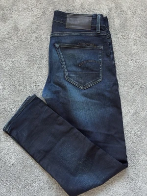 Mörkblå jeans från G-Star RAW - Säljer ett par sköna jeans från Gstar raw. Jeansen är slimfit med en schysst mörkblå tvätt. Dem är i storleken 28/30 och modellen på bild 2 är ca 172cm lång. Mitt pris är endast 99kr
