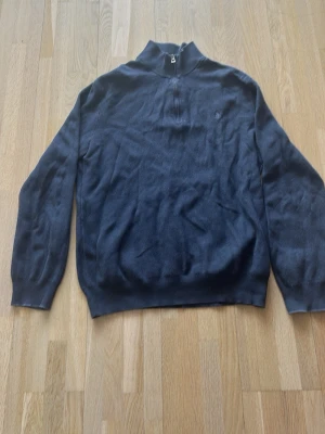 Mörkblå stickad tröja från Polo Ralph Lauren - Mörkblå stickad tröja med halv dragkedja och hög krage. Tröjan har långa ärmar och ribbade muddar vid ärmslut och nederkant. Enkel och stilren design, perfekt för lager på lager. Liten broderad logga på bröstet. Tröjan sitter mer som M än L enligt mig 