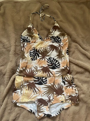  tankini/bikini - Snygg tankini med tropiskt bladmotiv i beige, brunt, svart och vitt. Aldrig använd! Storlek 42/44 i underdelen och överdelen storlek 46/48 men den passar mig som är storlek M så den är mindre i storlek. 