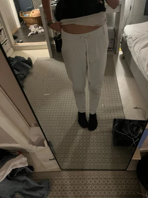 Vita mjukisbyxor med dragsko - Säljer ett par vita mjukisbyxor med dragsko i midjan och smal passform. Byxorna har resår i midjan och vid bensluten för en skön och avslappnad look. Perfekta för chill dagar hemma eller när du vill vara bekväm men ändå se snygg ut.