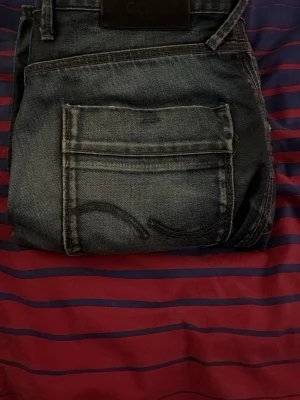 Mörkblå jeans från Cheap Monday - Säljer ett par mörkblå jeans från Cheap Monday med raka ben och slitna detaljer vid bensluten. Jeansen har klassiska bakfickor med broderad söm och är gjorda i denim. Perfekta för en avslappnad och cool stil. Ett litet hål vid bakfickan men inget som syns när de är på! W31 L32