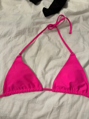 Rosa trekantsbikini med knyt - Snygg trekantsbikini i starkt rosa färg med tunna band och knyt i nacken. Perfekt för soliga dagar på stranden eller vid poolen. Enkel och stilren design som ger en fräsch look.