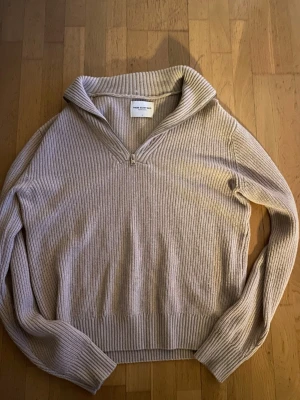 Beige stickad tröja med dragkedja - Säljer en beige stickad tröja från These Glory Days. Tröjan har en ribbad struktur, lång ärm och en snygg krage med kort dragkedja framtill. Passar S och M möjligtvis även L. Aldrig använd 