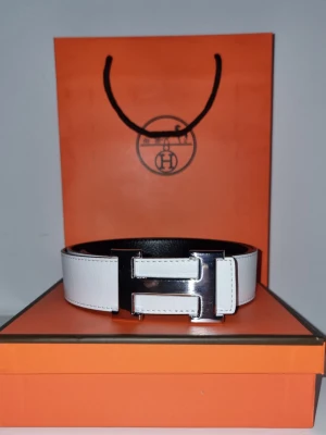 H bälte - Snyggt vitt skärp från H med ikoniskt H format spänne i silverfärgad metall. Bältet är gjort i skinn och har en stilren, modern look som passar till många outfits. Kommer i originalförpackning och med H påse.