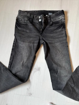 Bootcut jeans från H&M, svartgrå med fickor bak. storlek 164!!! - Bootcut jeans från H&M i svartgrå tvätt med låg midja och justerbar midja och fickor där bak. Klassisk femficksmodell med dragkedja och knapp framtill. Snyggt slitna detaljer och stretchigt material för skön passform. Storlek 164!!!