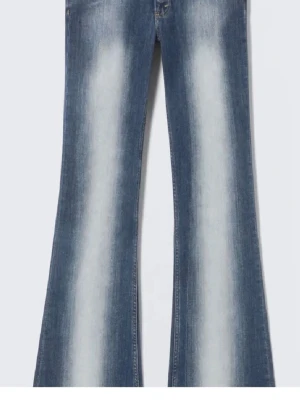 Blå utsvängda jeans med slitningar - Säljer ett par blå jeans med tydliga slitningar och utsvängda ben. Jeansen har en ljus tvätt längs framsidan och klassisk femficksdesign. Perfekta för dig som gillar retrostil och vill sticka ut med en cool siluett.