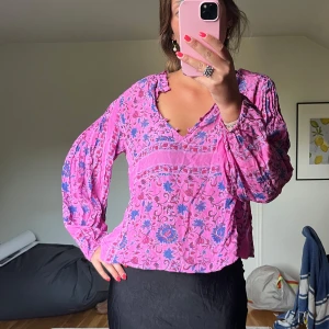 Rosa blommig blus med v-ringning - Superfin rosa blus med blått och lila blommönster, v-ringad hals och långa puffiga ärmar. 