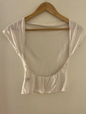 Vit croppad topp med öppen rygg - Säljer en vit croppad topp i bomull med korta ärmar och en riktigt djup, öppen rygg. Perfekt för dig som vill ha en enkel men ändå statement topp till sommaren. Sitter tajt och har en clean look utan mönster eller detaljer.
