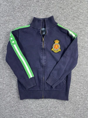 Polo Ralph Lauren Vintage Zip-Tröja – “Crested Knit” – S (sitter som XS) - äljer en vintage Polo Ralph Lauren stickad zip-tröja i klassisk preppy look. Marinblå bas med kontrasterande gröna/randiga detaljer och vintage crest-brodyr ger en unik retrovibe. 📌 Storlek: S (sitter mer som XS) 📌 Klassisk, mjuk stickad tröja 📌 Full dragkedja & ribbad krage 📌 Perfekt till jeans, chinos eller layered outfits 📏 Mått visas i bilderna 🔎 Eventuella detaljer/slitage visas i bilderna 💸 Följ mig så får du 10% rabatt! Snabb frakt & seriös säljare. 