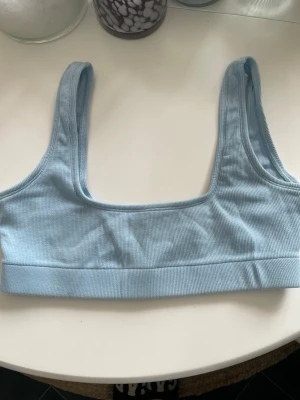Ljusblå ribbad bralette - Säljer en ljusblå ribbad bralette med breda axelband och fyrkantig urringning. Bh:n är mjuk och utan bygel, perfekt för en avslappnad stil. Materialet är stretchigt och bekvämt, troligen bomullsblandning.