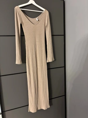Beige ribbad långklänning Nelly - Säljer en beige ribbad långklänning från Nelly i storlek XS. Klänningen har lång ärm, v-ringad hals och är figurnära med stretchigt material. Perfekt för dig som gillar stilrena och enkla plagg med en modern touch.