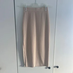 Beige ribbad kjol - Säljer en beige ribbad kjol med smal passform. Kjolen har en stilren look och är perfekt för dig som gillar minimalistisk stil. Materialet är stretchigt och bekvämt, vilket gör den enkel att bära hela dagen. Hittade inga lappar i den men tror den är XS!