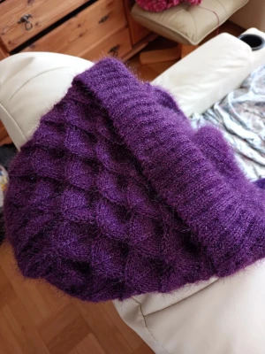 Lila stickad mössa med struktur - Mysig lila stickad mössa med strukturmönster och mjukt grått fleecefoder på insidan. Perfekt för kalla dagar och ger en cool, avslappnad look. Ingen synlig logga eller märke. Materialet är fluffigt och värmande.