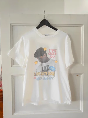 CarneBolente T-shirt  - Vit t-shirt från Carne Bolente med färgglatt tryck framtill som visar en person, stjärnor och texten 'I'VE GOT IT!', '1-800-CUTE DUDE' och 'HOLA GUAPO!'. T-shirten har rund hals och korta ärmar. Perfekt för dig som gillar grafiska motiv och en avslappnad stil.