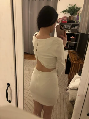 Lulus Vit kort klänning med öppen rygg - Säljer en UNIK Lulus  vit, figurnära kort klänning med långa ärmar och unik öppen rygg med dekorativa knappar. Strl M på den men passar super på mig som är xs/s. Obs har vikt upp den ca 5cm lite då den är lite lång på mig som är 1.57. Perfekt till studenten🩷 Använd gärna köp nu