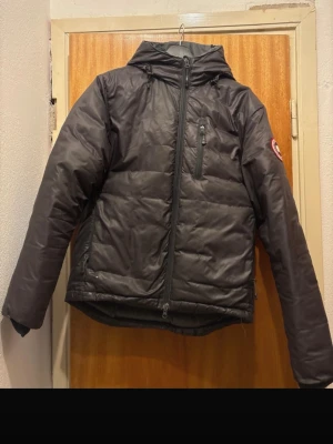  Canada Goose lodge jacket grey - Säljer en grå jacka från Canada Goose lodge jacket från johnells. Jackan har en bröstficka med dragkedja och den klassiska Canada Goose-loggan på ärmen. Perfekt för kalla vinterdagar och riktigt snygg streetstil. Den ända skavanken är ett litet litet ”hål” precis vid höger ficka.