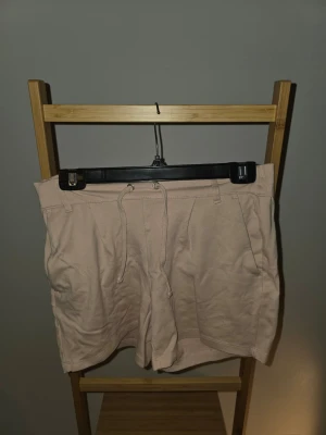 Beiga shorts med snörning - Snygga beiga shorts med snörning i midjan och fickor fram. De har en avslappnad passform och är perfekta för varma dagar. Gjorda i mjukt bomullsmaterial för extra komfort.