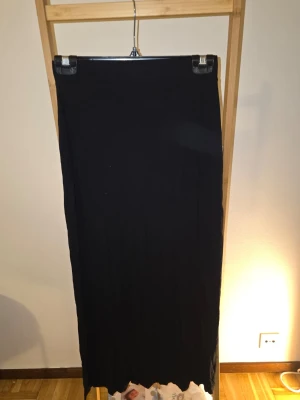 Svart långkjol i bomull - En enkel och stilren svart långkjol i mjukt bomullstyg. Kjolen har rak passform och är perfekt för dig som gillar minimalistisk stil. Inga synliga detaljer eller mönster, bara klassiskt svart. Står tyvärr ingen storlek men passar mig som är S.