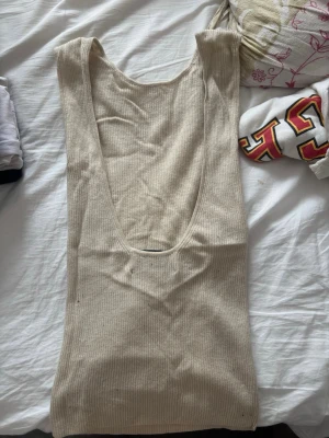 Beige ribbad ärmlös linnetopp - Snygg beige ribbad linnetopp med öppetrygg. Toppen är ärmlös och har en tight passform som framhäver figuren. Perfekt att styla med jeans eller kjol för en enkel och trendig look.