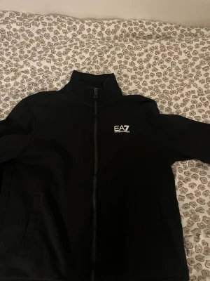 Svart kofta  från EA7 Emporio Armani.  - Snygg svart ziptröja från EA7 Emporio Armani med hög krage och vit logga på bröstet. Fantastik fin kofta, utan tvekan även oroligt bekväm. Den va för liten för mig!