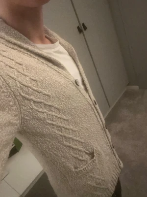 Beige kofta från Massimo Dutti - Säljer en beige stickad kofta från Massimo Dutti med snygg kabelstickad design och knappar framtill. Koftan har två fickor och en mjuk, grovstickad känsla. Perfekt för lager på lager och riktigt skön att ha på sig. As fet färg och passform och passar till det mesta 