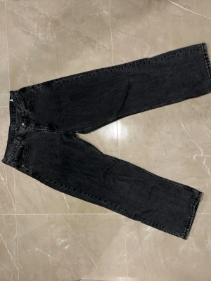 Svarta raka jeans med fem fickor - Säljer ett par svarta jeans med rak passform och klassisk femficksdesign. Jeansen har normal midja och är tillverkade i ett robust denimtyg. Perfekta för en avslappnad och stilren look.