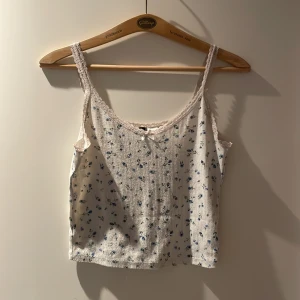Blommig spetslinnetopp  - Supersöt linne-topp i vitt från H&M med små blå blommor, spetskant och en liten rosett framtill. Tunt ribbat material och smala axelband. 