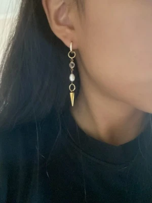 Guldpläterade örhängen med sötvattenpärla och konformad avslutning - Priset avser ett par örhängen. Matchande halsband finns i en separat annons  Finns även i silverfärg   Material: Guldpläterat rostfritt stål och sötvattenpärla Längd: ca 6,5 cm Nickelfria och handgjorda