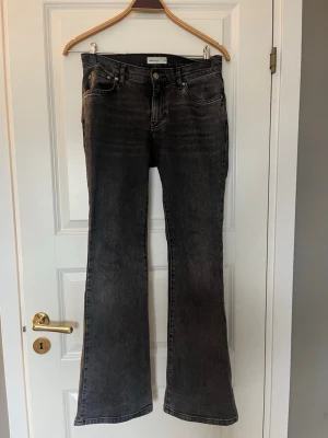 Svarta bootcut jeans från Gina Tricot - Säljer ett par svarta bootcut jeans från Gina Tricot med lätt tvättad look. Jeansen har fem fickor, låg midja och utsvängda ben. Klassisk knappgylf och bälteshällor. Perfekta för en trendig och avslappnad stil.