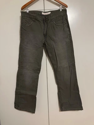 Grå raka, breda jeans med fem fickor - Säljer ett par vintage grå jeans med rak passform och klassisk femficksdesign. Jeansen har normal midja och stängs med knapp och dragkedja. Materialet är denim i bomull och färgen är en tvättad grå ton. Perfekta för en avslappnad och stilren look. Passar 32-34