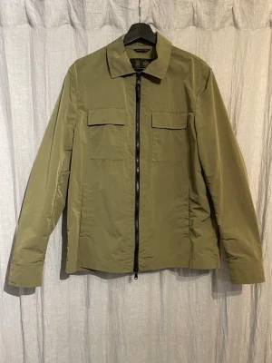 Morris vindjacka - Stilren olivgrön vindjacka från Morris. Funkar perfekt för våren då materialet liknar det av en regnjacka. Köpt för ett år sen på Hugos i Karlstad men används inte längre. Stoleken är small men passar även medium.