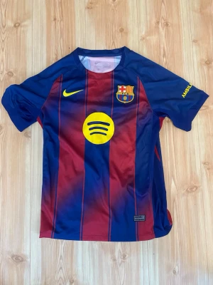 FC Barcelona matchtröja Nike - Säljer en FC Barcelona matchtröja från Nike i klassiska blå och röda färger med gula detaljer. Tröjan har klubbmärke på bröstet, Spotify-logga och Nike Swoosh. Tillverkad i lätt och ventilerande material, perfekt för fotboll eller träning.