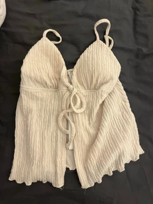 Beige linnetopp från New yorker  - Supersöt beige linnetopp från New yorker med smala axelband och knyt framtill. Toppen har en vågig, strukturerad yta och lätt utsvängd passform. Perfekt för varma dagar och enkel att styla med jeans eller kjol.