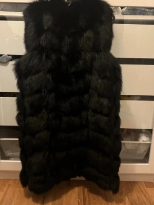 Svart lång väst från feminina - Snygg svart lång pälsväst, fluffig. Västen har en öppen front och är helfodrad för extra komfort. Perfekt för dig som vill ha en trendig och lyxig look.