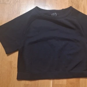 Svart croppad träningstopp Aim'n - Snygg svart croppad träningstopp från Aim'n med korta ärmar och meshdetaljer på sidorna. Toppen har rund halsringning och är tillverkad i ett stretchigt syntetmaterial som andas. Perfekt för gymmet eller yoga.