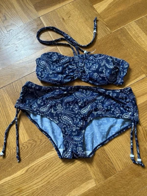 Mörkblå bandeau bikini med paisleymönster - Snygg mörkblå bandeau bikini med vitt paisleymönster. Inläggen i toppen går att ta ur.