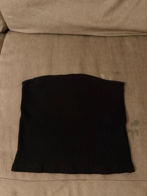Svart ribbad tubtopp från Pieces - Säljer en svart ribbad tubtopp från Pieces. Toppen är axelbandslös och har en enkel, tight passform som sitter snyggt. Perfekt att styla med jeans eller kjol för en clean look.