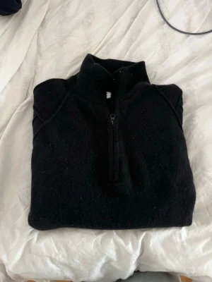 Svart halvzip stickad tröja cp company - Svart stickad tröja med halvzip och hög krage. Tröjan har långa ärmar och ribbade muddar vid ärmslut och nederkant. Perfekt för lager-på-lager och enkel att matcha med olika outfits.
