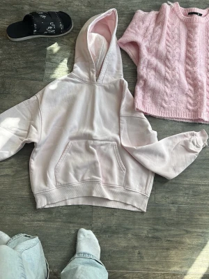 Ljusrosa hoodie med huva och flätad ljus rosa tröja. - Gina tricot och lager. Säljer en ljusrosa hoodie med stor huva och magficka. Hoodien har en avslappnad passform och ribbade muddar vid ärmar och nederkant. Perfekt för en chill och bekväm stil. Materialet känns mjukt och skönt mot huden.