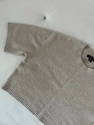 Beige stickad kortärmad tröja - Säljer en beige stickad tröja från Amisu med korta ärmar och rund hals. Tröjan har ribbstickade muddar vid ärmslut, hals och nederkant. Perfekt för lager-på-lager och enkel att matcha med olika outfits.🤩💞( mycket mindre i verkligheten) 