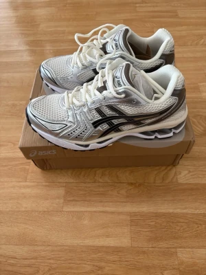 ASICS vita sneakers med silverdetaljer - Snygga sneakers från ASICS i vitt med silvriga och svarta detaljer. Skorna har en sportig design med mesh-överdel och klassisk snörning. Perfekta för dig som gillar streetstyle och vill ha bekväma skor med cool look.